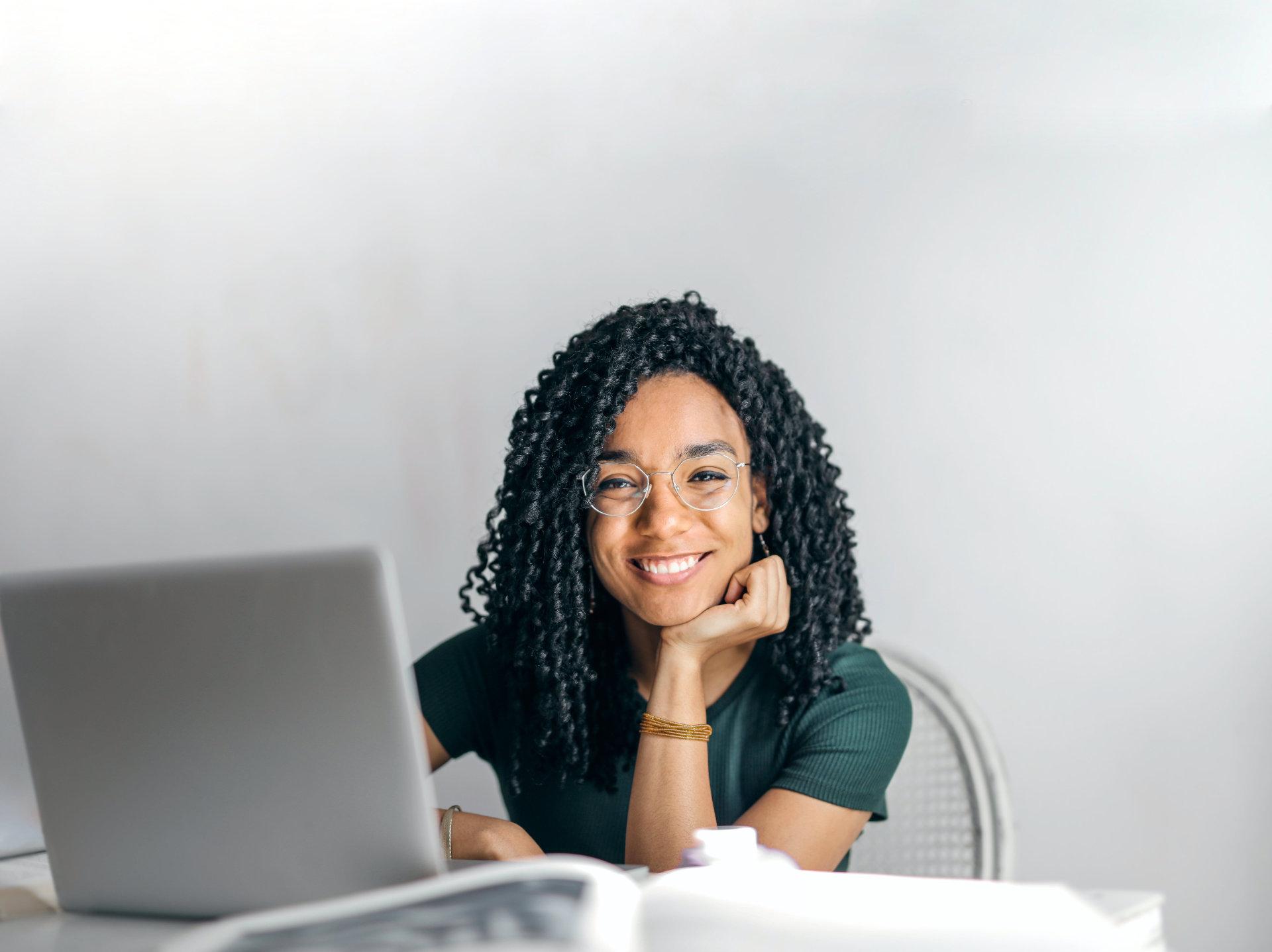 Happy ethnic woman sitting at table with laptop