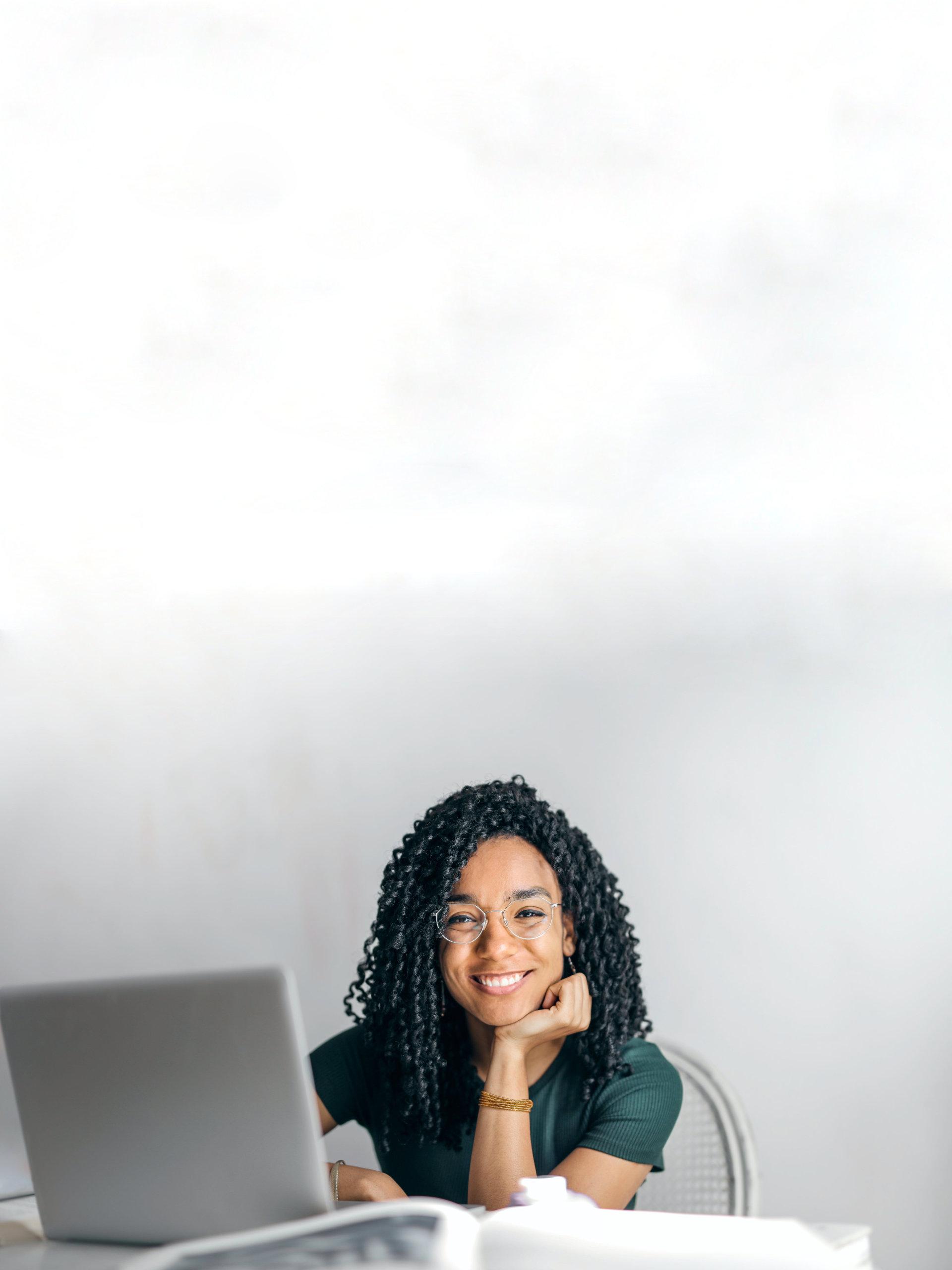 Happy ethnic woman sitting at table with laptop