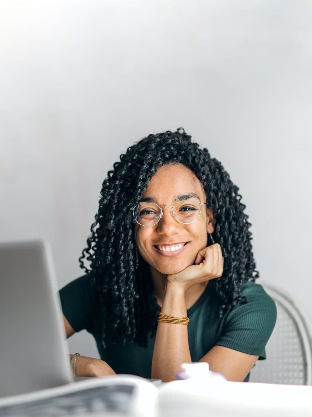 Happy ethnic woman sitting at table with laptop