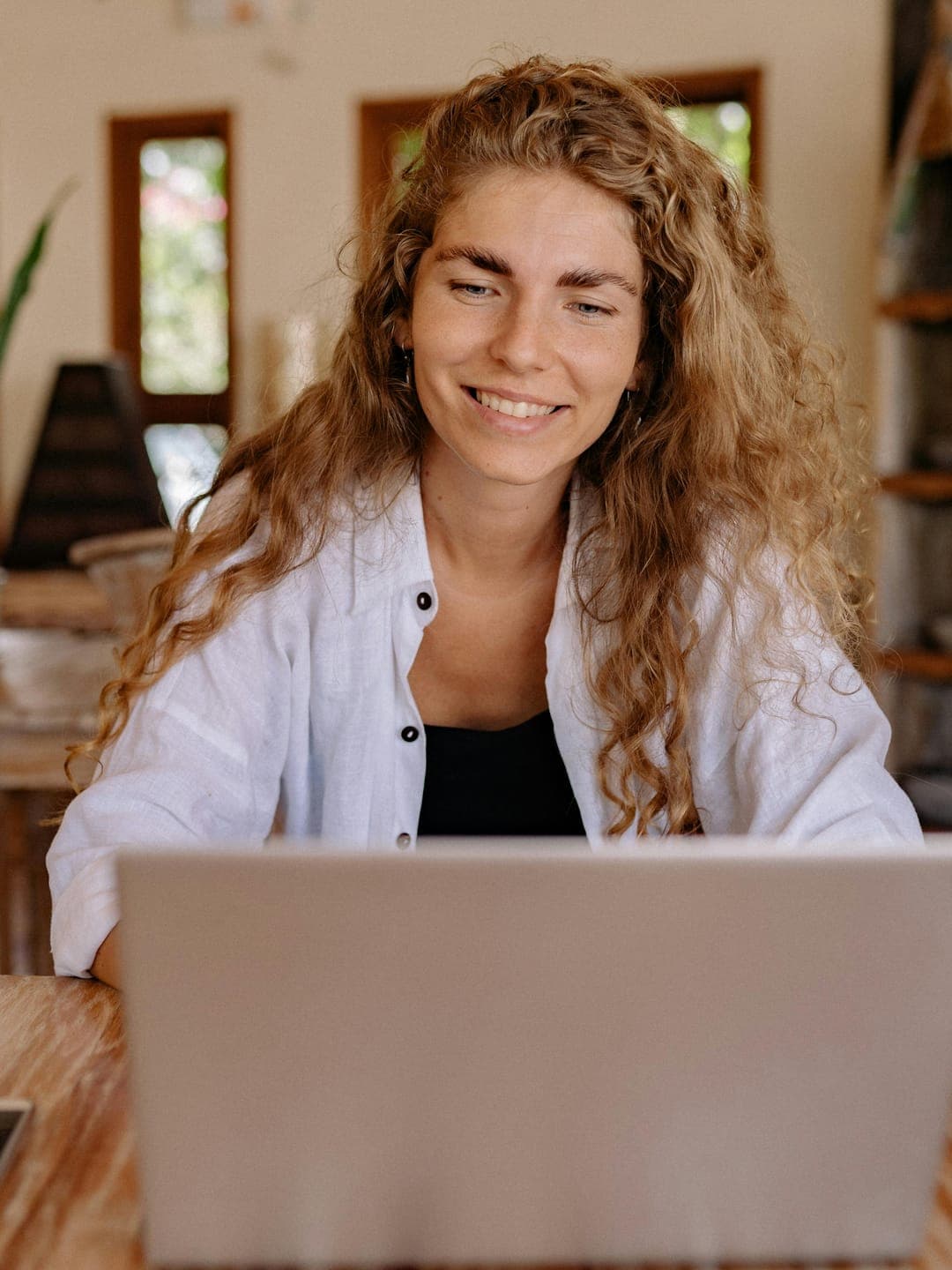 Happy ethnic woman sitting at table with laptop