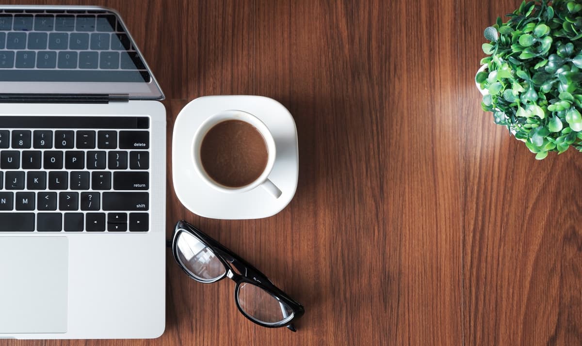 A laptop, coffee and a plant on a wooden desk symbolizing psychological online counseling from home